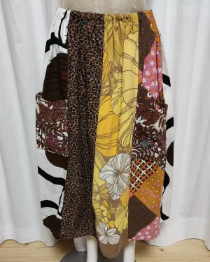 Kjol i patchwork med färger i brunt, beige, orange och gult. Bomull. Kjolen sitter på en kläddocka. Kjolen är sydd av slow fashion-företaget Skamlös Design