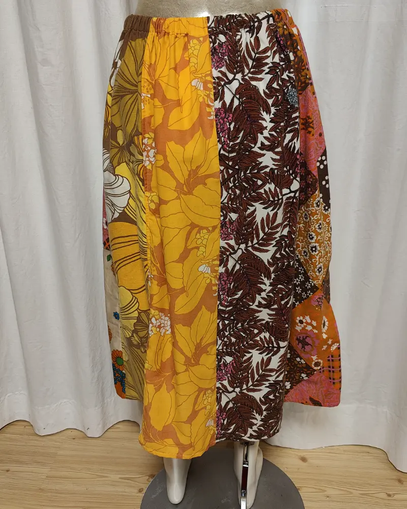 Kjol i patchwork med färger i brunt, beige, orange och gult. Bomull. Kjolen sitter på en kläddocka. Kjolen är sydd av slow fashion-företaget Skamlös Design