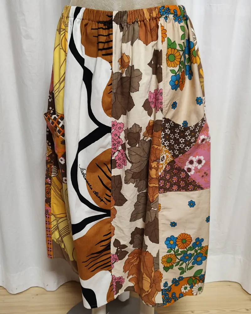 Kjol i patchwork med färger i brunt, beige, orange och gult. Bomull. Kjolen sitter på en kläddocka. Kjolen är sydd av slow fashion-företaget Skamlös Design