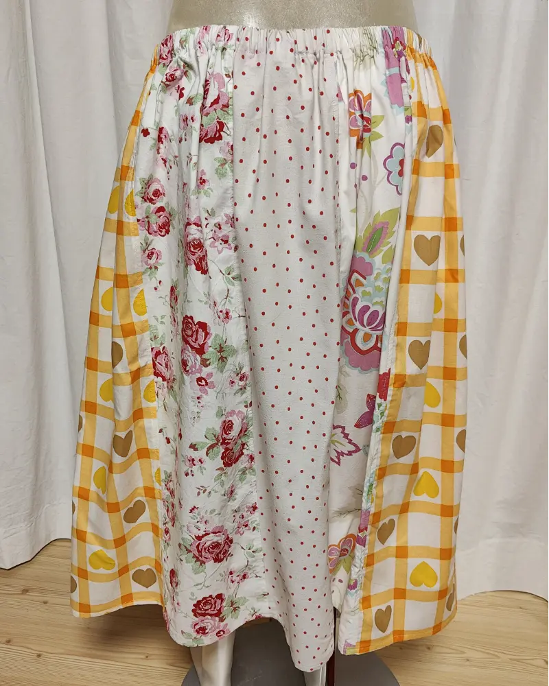 Kjol i patchwork med vit och beige ochmönste ri rosa samt orange. Bomull. Kjolen sitter på en kläddocka. Kjolen är sydd av slow fashion-företaget Skamlös Design