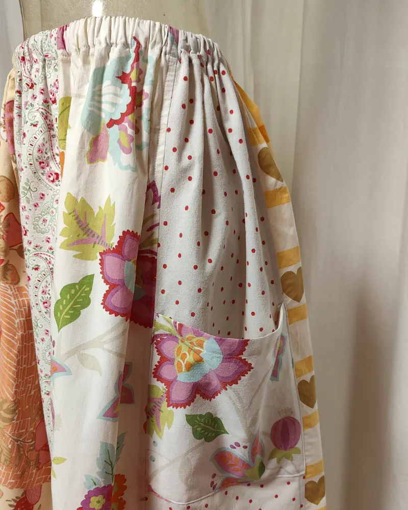 Kjol i patchwork med vit och beige ochmönste ri rosa samt orange. Bomull. Kjolen sitter på en kläddocka. Kjolen är sydd av slow fashion-företaget Skamlös Design