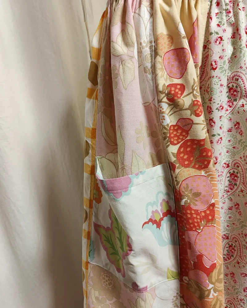 Kjol i patchwork med vit och beige ochmönste ri rosa samt orange. Bomull. Kjolen sitter på en kläddocka. Kjolen är sydd av slow fashion-företaget Skamlös Design