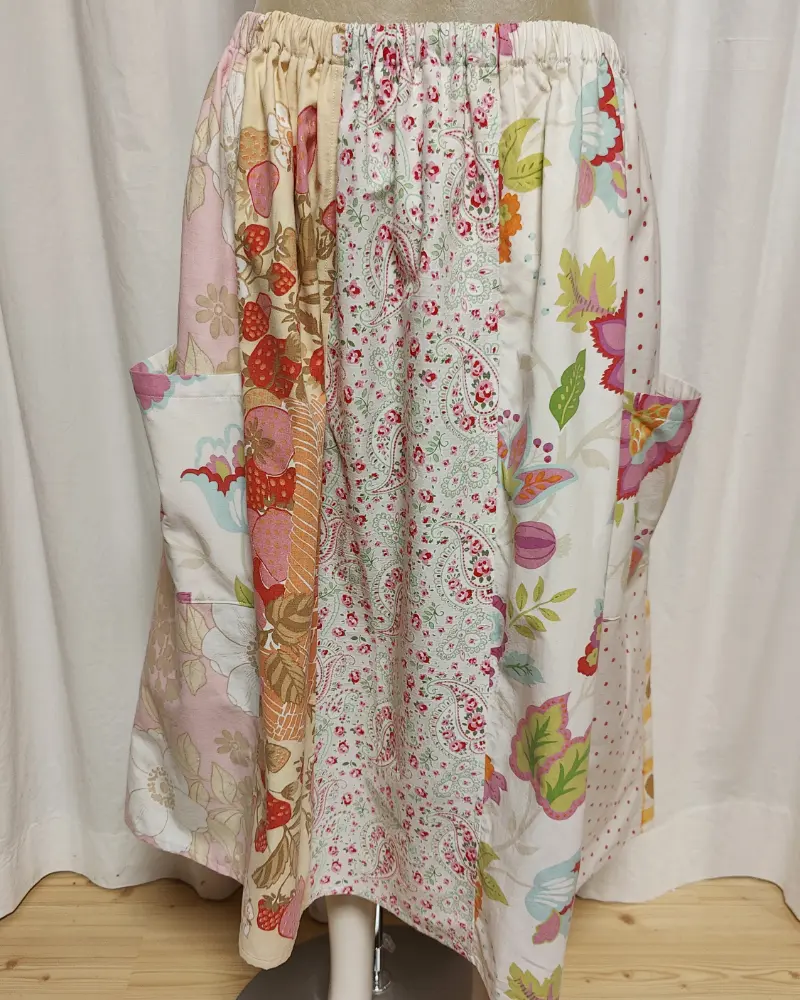 Kjol i patchwork med vit och beige ochmönste ri rosa samt orange. Bomull. Kjolen sitter på en kläddocka. Kjolen är sydd av slow fashion-företaget Skamlös Design
