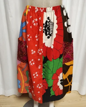 Kjol i patchwork med röda, rosa och orange färger. Bomull. Kjolen sitter på en kläddocka. Kjolen är sydd av slow fashion-företaget Skamlös Design