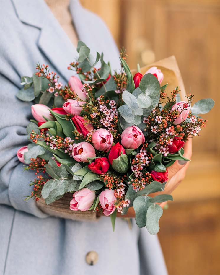 Ljuvlig bukett med röda och rosa tulpaner tillsammans med eucalyptusblad och dekoratinsgrönt.