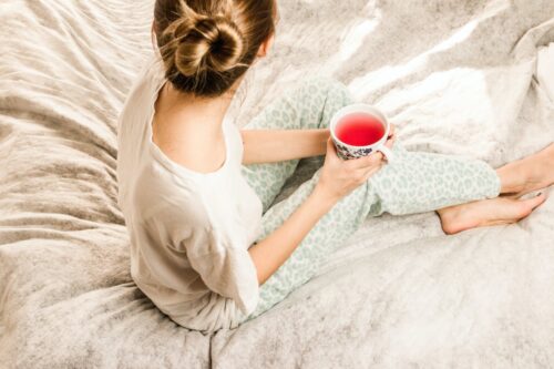 aerial view photography of woman sitting on blanket while holding mug filled with pink liquid looking sideward