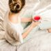 aerial view photography of woman sitting on blanket while holding mug filled with pink liquid looking sideward