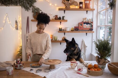 woman putting christmas cookies on a tray and her dog watching her