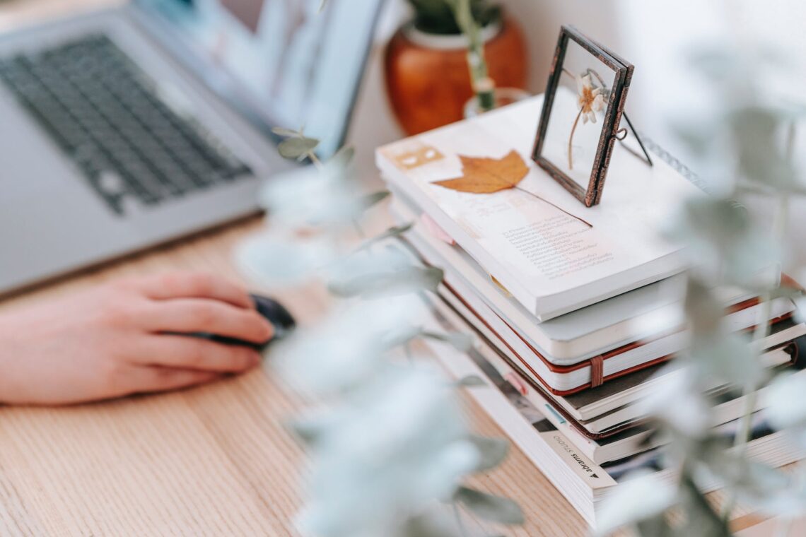 crop remote employee working on laptop against books at home