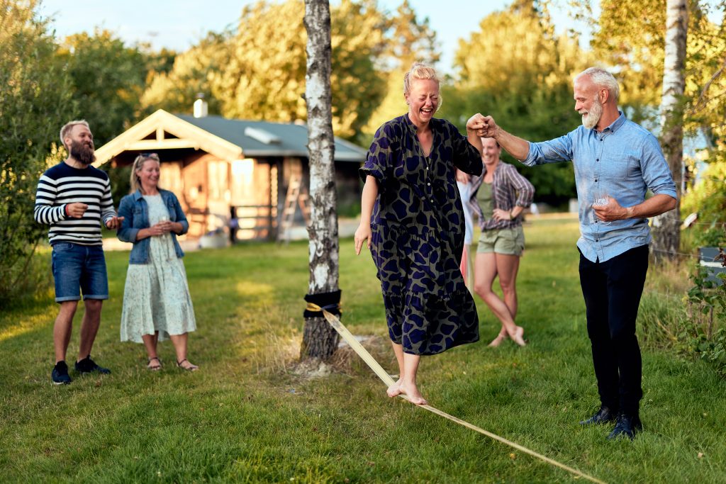Laughing mature woman walking along a slack line with family watching in summer