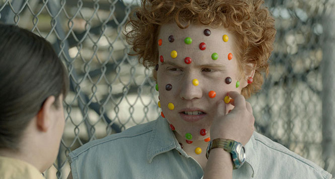 Child with Skittles sweets stuck to their face