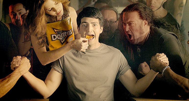 Man arm-wrestling two people simultaneously whilst being fed Doritos