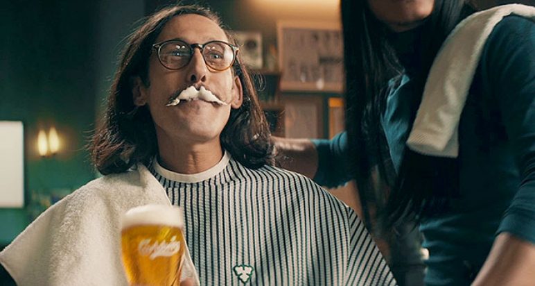 Man in barber's shop clutching pint of Carlsberg lager
