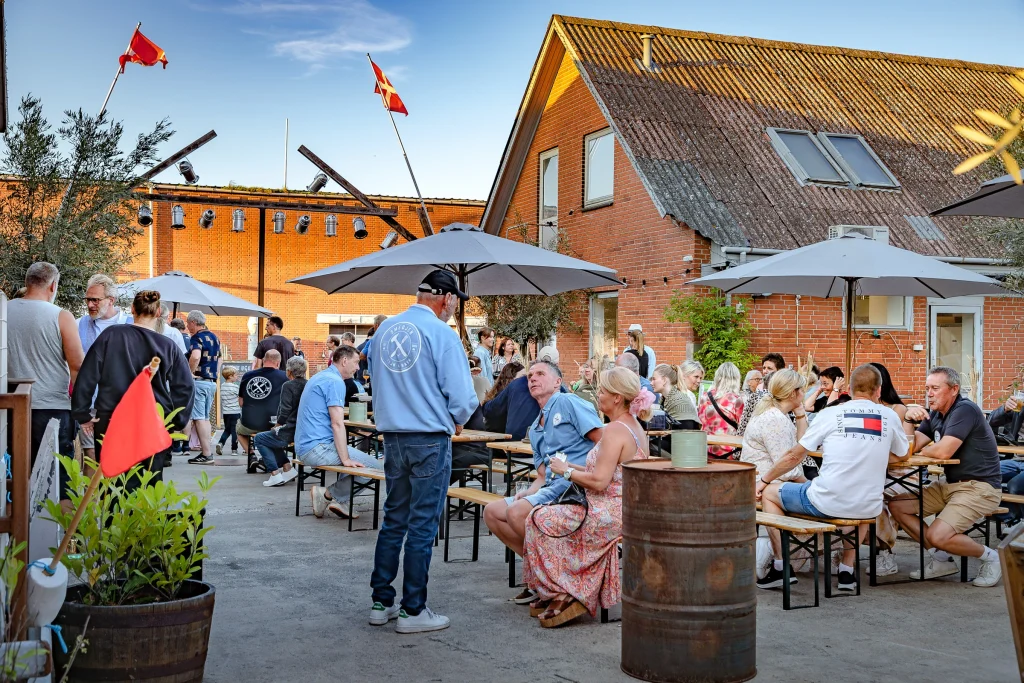 Udendørs aftenstemning foran Smedjen Street Food, hvor mennesker nyder drinks og samtaler i sent solskinsvejr.