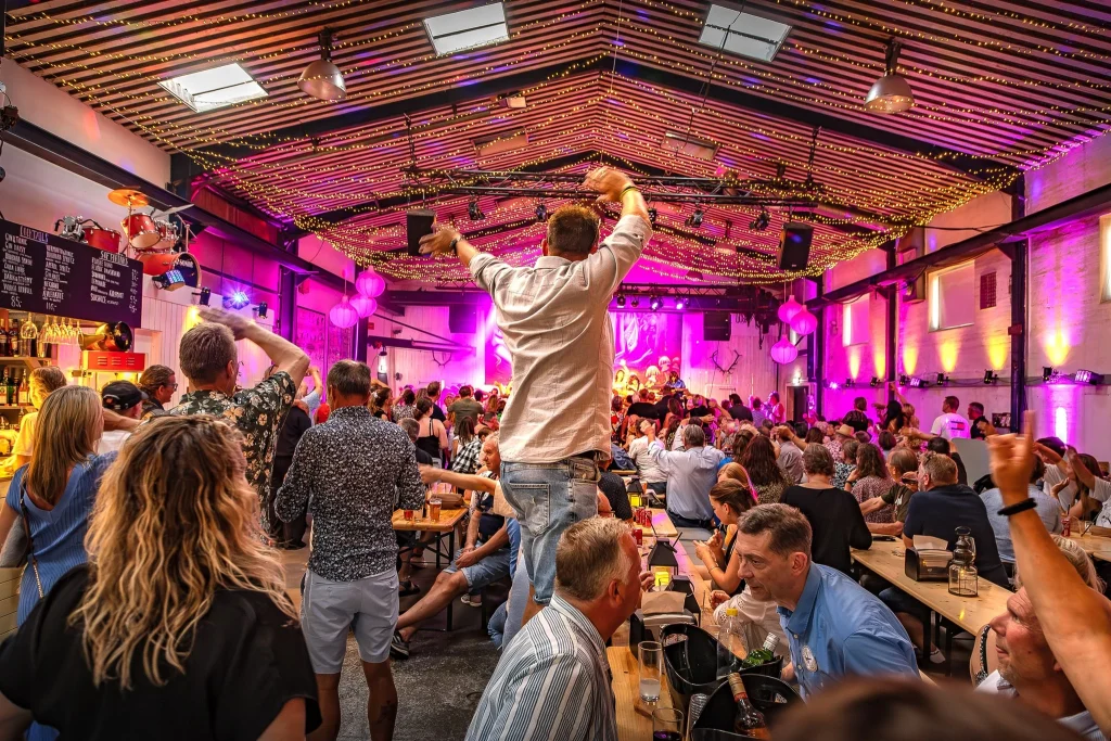 Indendørs aftenstemning i Smedjen Street Food, hvor mennesker nyder en koncert i farverigt lys.
