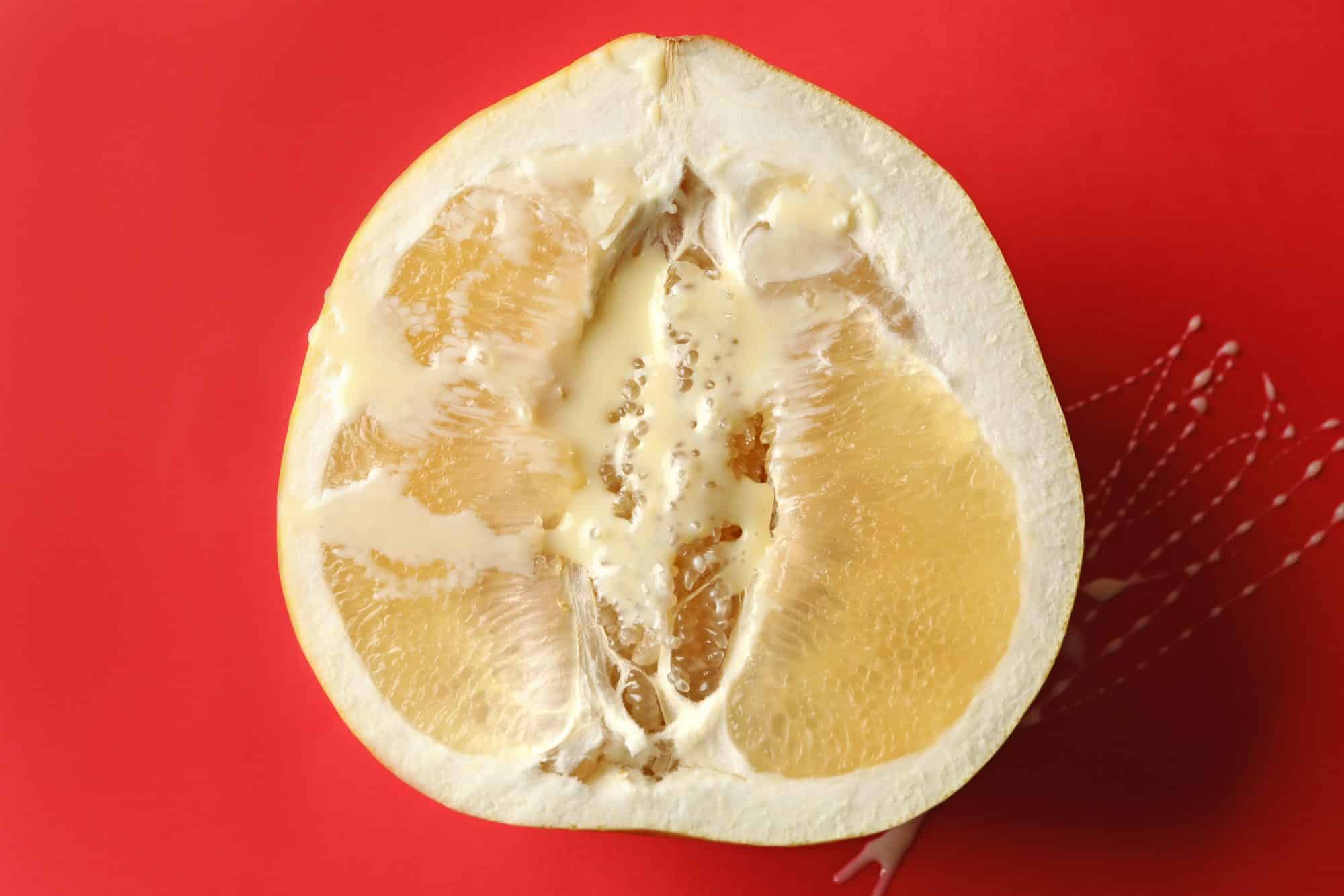 Half of ripe pomelo fruit with condensed milk on red background