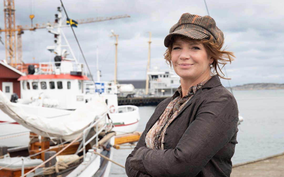 Maria Larsson står på en brygga. I bakgrunden syns en skuta och fiskebåtar.