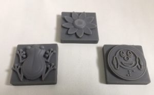 3D printed grid tiles of frog, flower, and Ballyland coin.