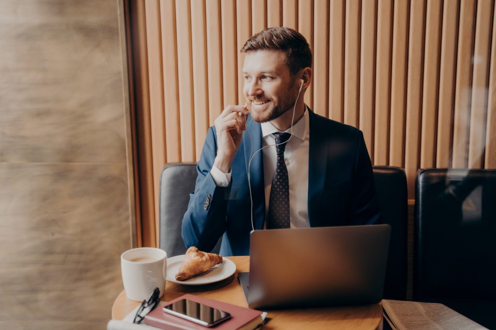 Male investor in blue suit talking with business partner online through laptop in restaurant