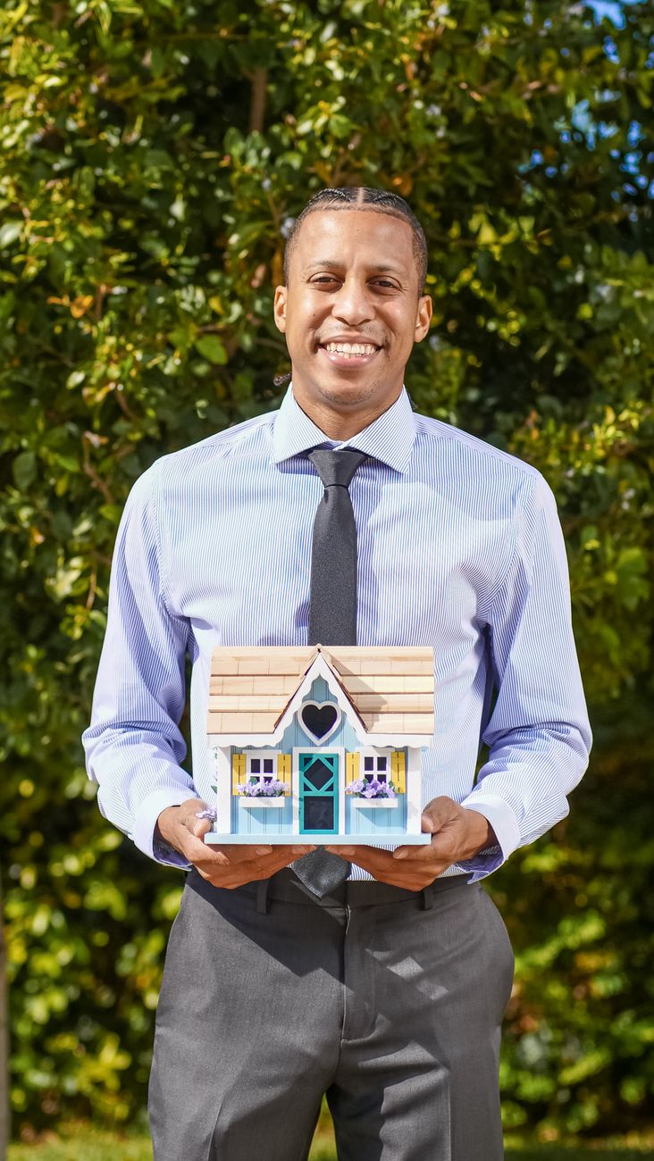 man in blue dress shirt holding a miniature wooden house