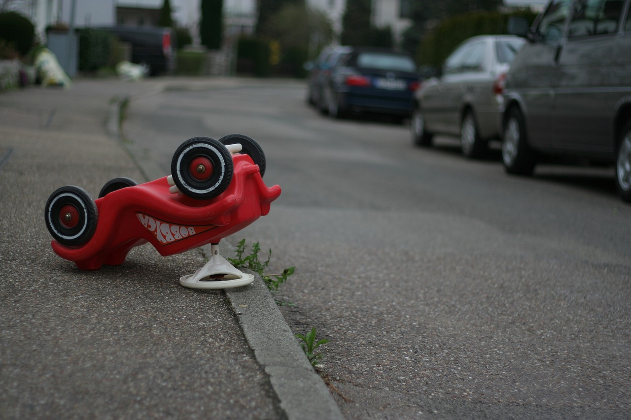 ein rotes Bobby Car liegt auf dem Kopf auf einem Gehweg und soll einen Unfall symbolisieren.