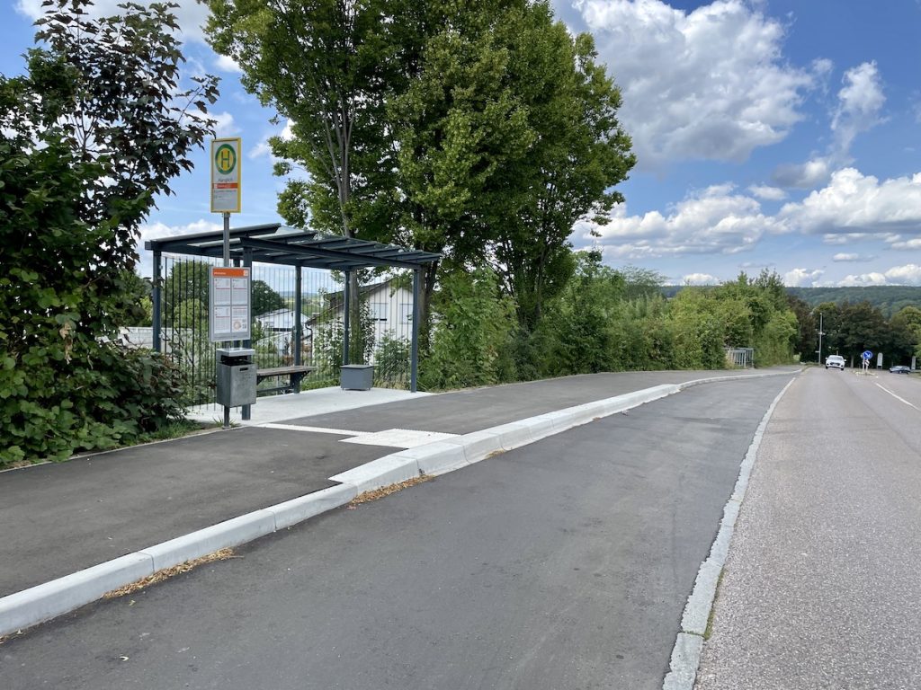 Eine Bushaltestelle am Straßenrand mit speziellen Busbordsteinen und Blindenleitstreifen.