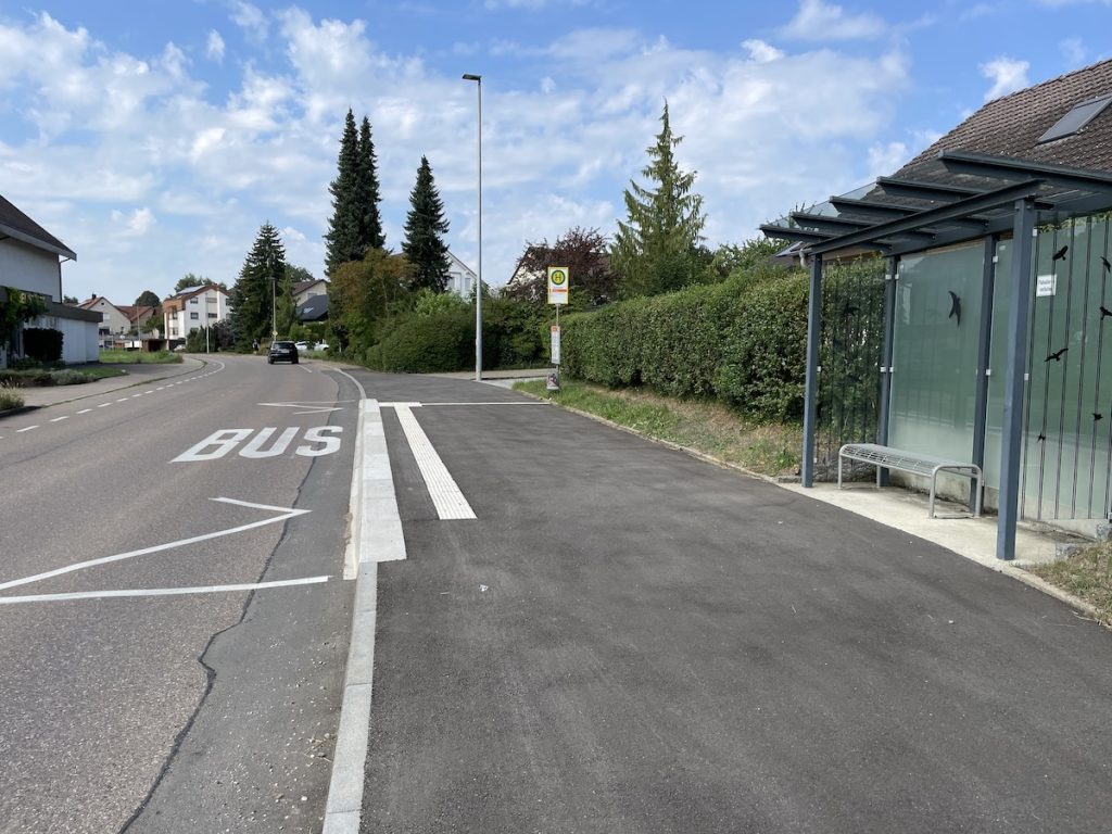 Eine Bushaltestelle am Straßenrand mit speziellen Busbordsteinen und Blindenleitstreifen.