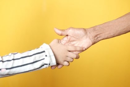 Building Trust a person holding a child's hand with a yellow background