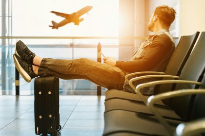 Unveiling the Secrets of Budget Travel: Maximize Your Adventures Without Breaking the Bank Travel man sitting on gang chair with feet on luggage looking at airplane