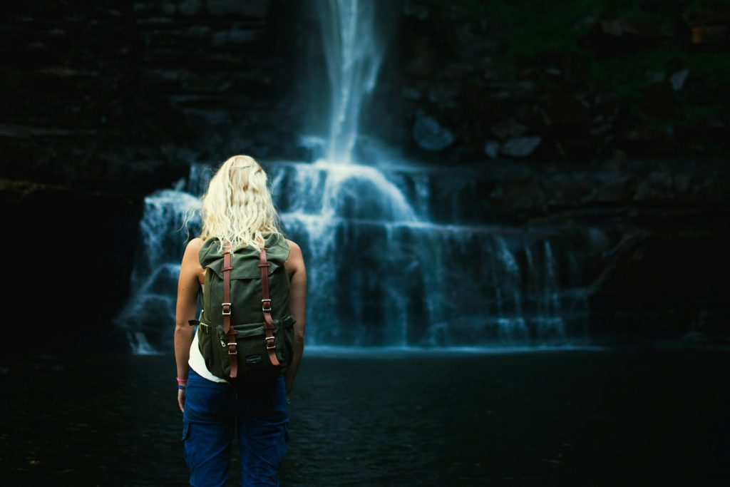 shallow focus photography of woman with backpack in front of water falls Pack light Mastering the Art of Travel Photography