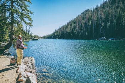 man standing on rock on front of lake surrounded with trees at daytime