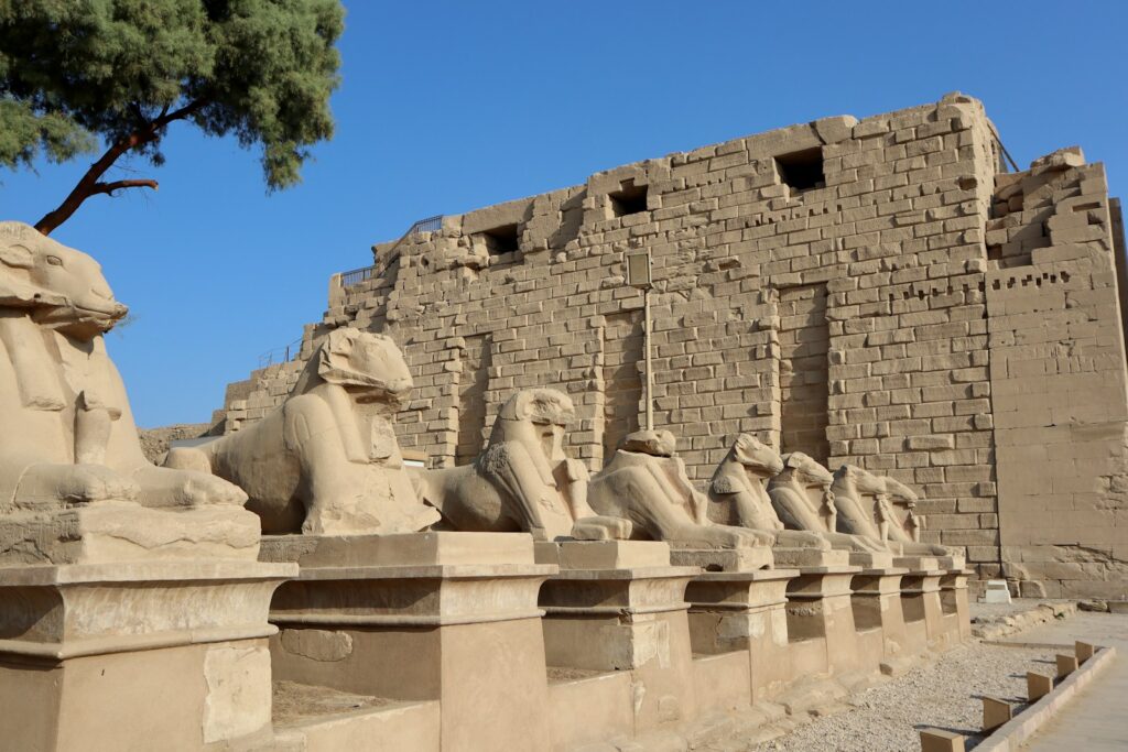 a row of sphinx statues in front of a stone wall Karnak Temple Complex Spiritual Journey