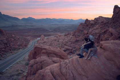 two people sitting on top of a large rock