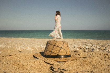 woman walking near seashore and brown and gray hat on brown sand