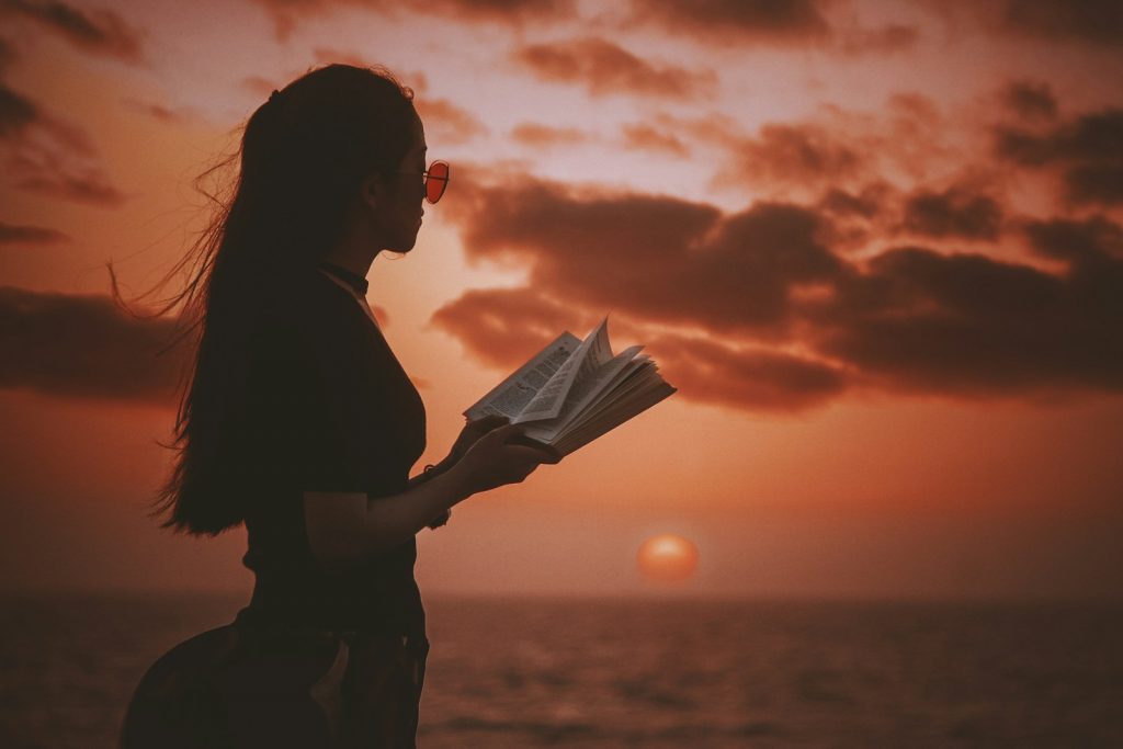woman holding book while looking at body of water during golden hour Book Accommodation in Advance Embracing the Beauty