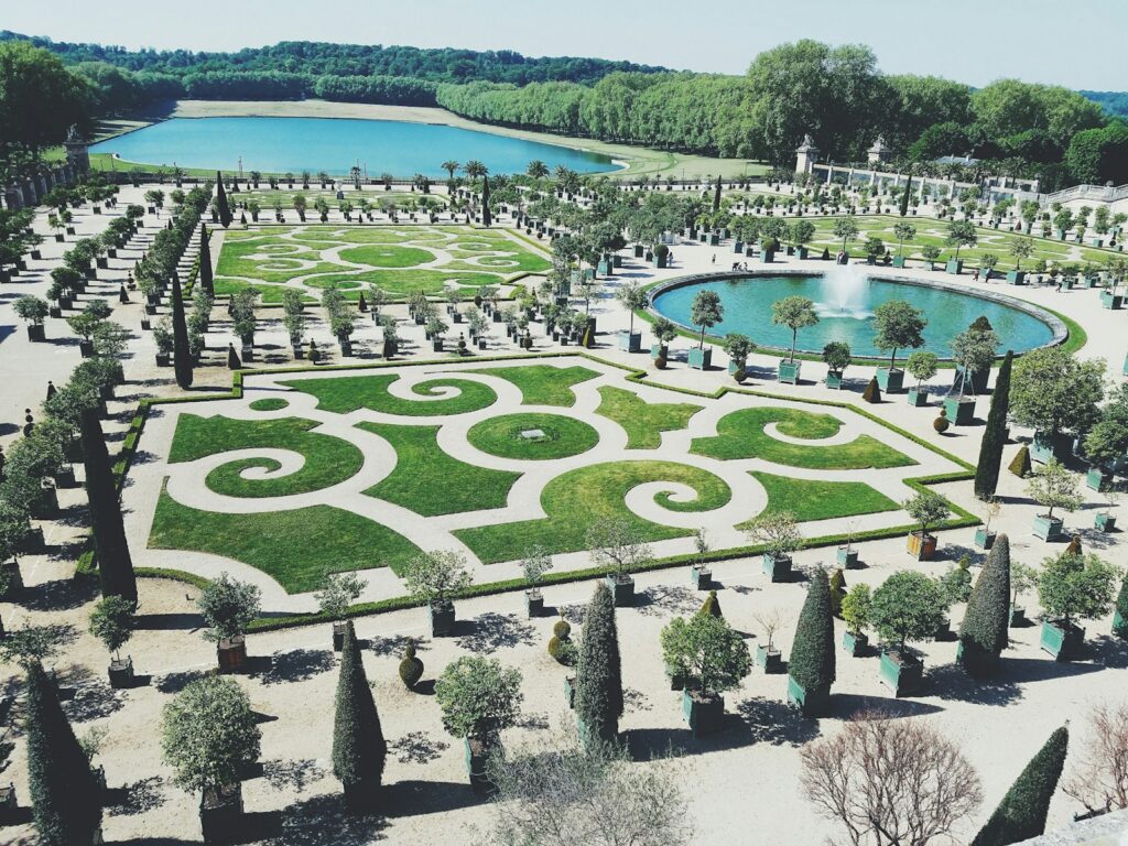green grass field near body of water during daytime Gardens of Versailles Famous Gardens and Parks
