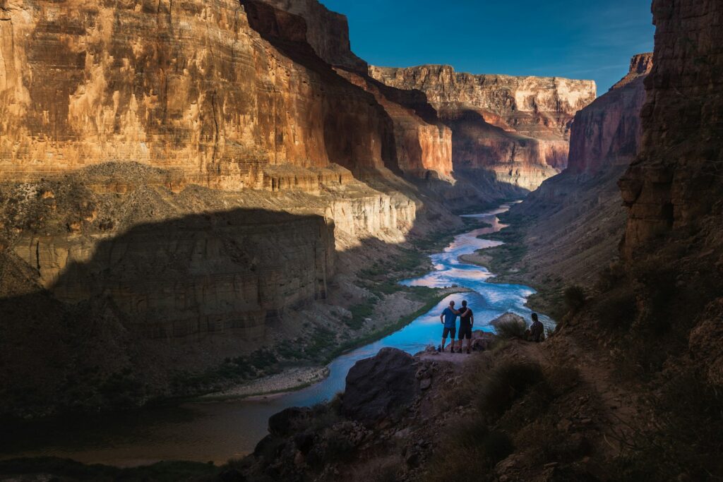 two person standing on rocks facing body of water Grand Canyon World's Largest Canyons