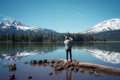 woman in white long sleeve shirt and blue denim jeans standing on brown log near lake