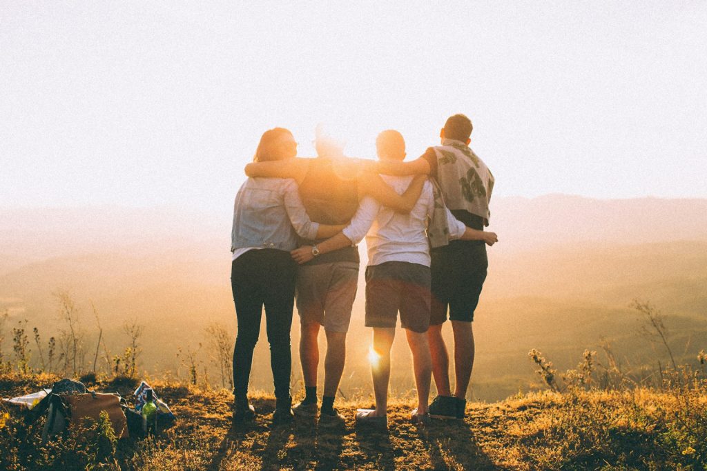 four person hands wrap around shoulders while looking at sunset Connection to Nature Roaming with Purpose