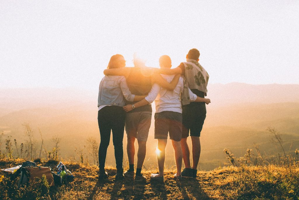 four person hands wrap around shoulders while looking at sunset The Future of Travel  Art and Architecture 