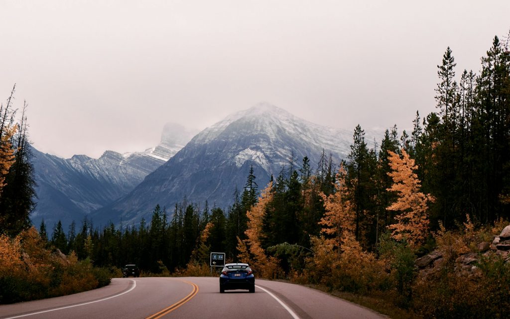 a car driving down a road with mountains in the background Icefields Parkway Unforgettable Road Trips