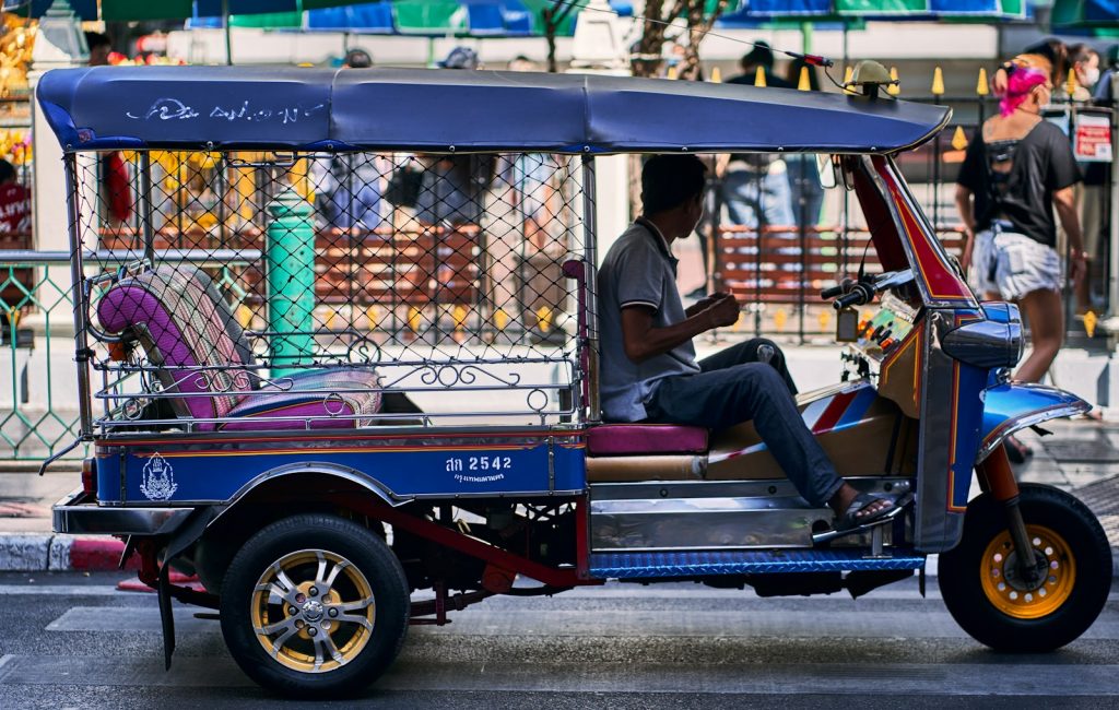 a man sitting on the back of a blue three wheeled vehicle Tuk-Tuks Beyond the Roads