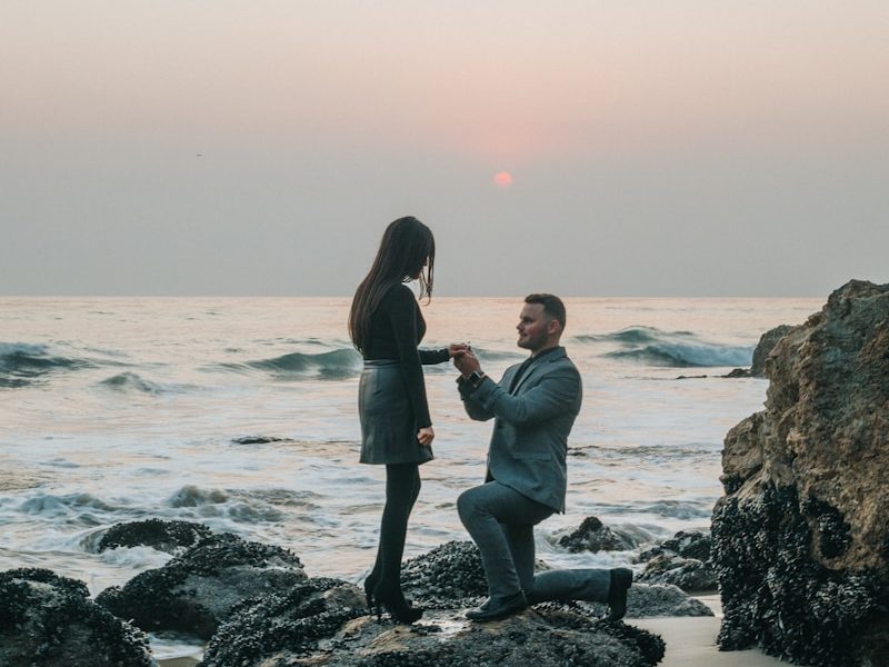 man kneeling in front of woman on rock at beach Private Sector Engagement Sustainable Tourism Initiatives