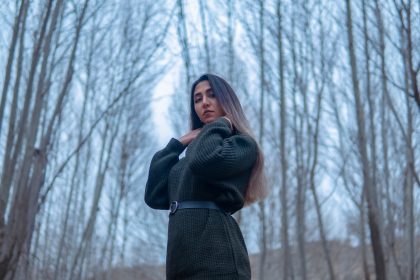 a woman standing in a forest with trees in the background