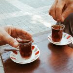 person holding clear glass mug with brown liquid