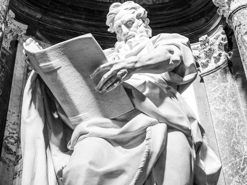 a statue of a man holding a book in front of a building Rich Storyline Jacksmith