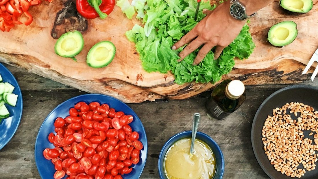 person slicing green vegetable in front of round ceramic plates with assorted sliced vegetables during daytime