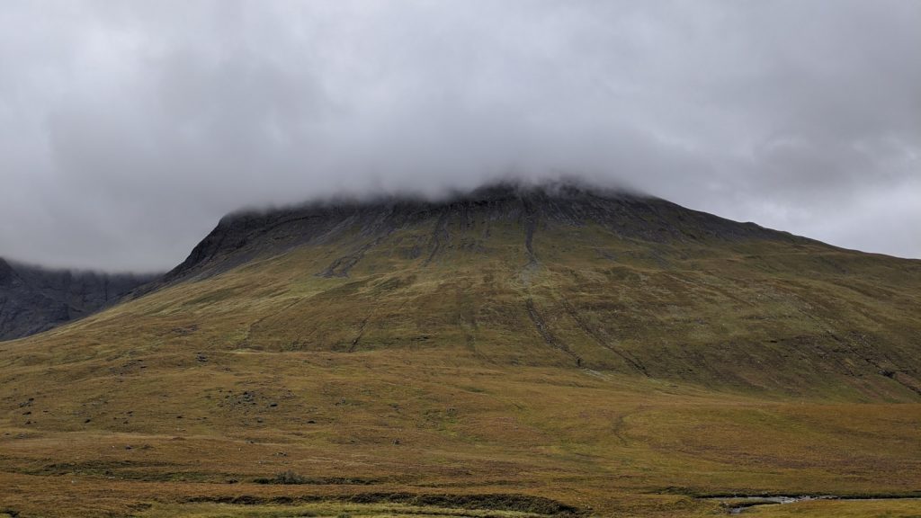 a mountain covered in grass and clouds on a cloudy day