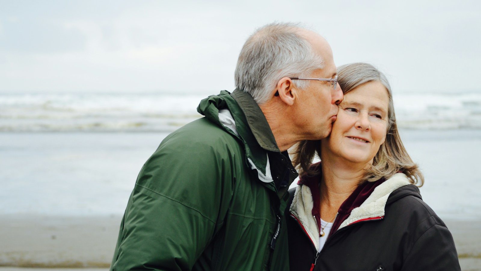 man kissing woman on check beside body of water