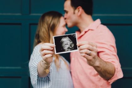 man kissing woman's forehead white holding ultrasound photo